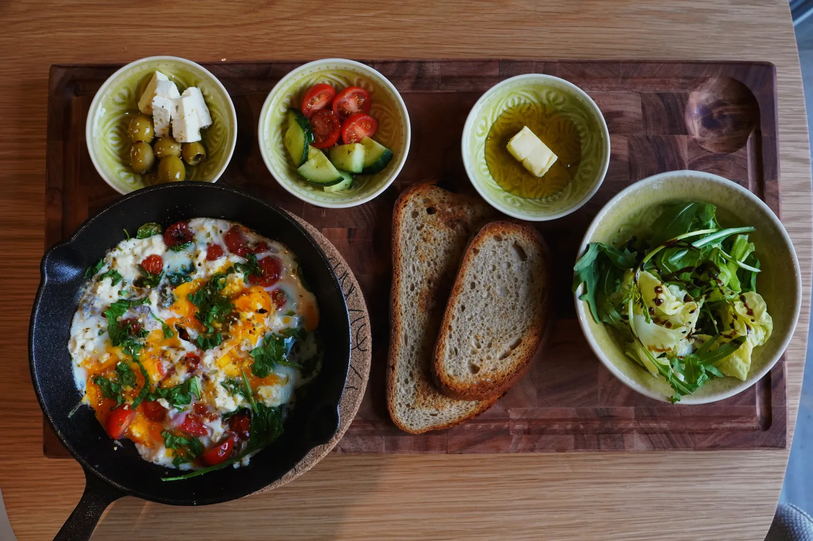 Eierpfanne mit Sauerteigbrot, Salat, Oliven, Feta und Tomaten auf dem Holzbrett